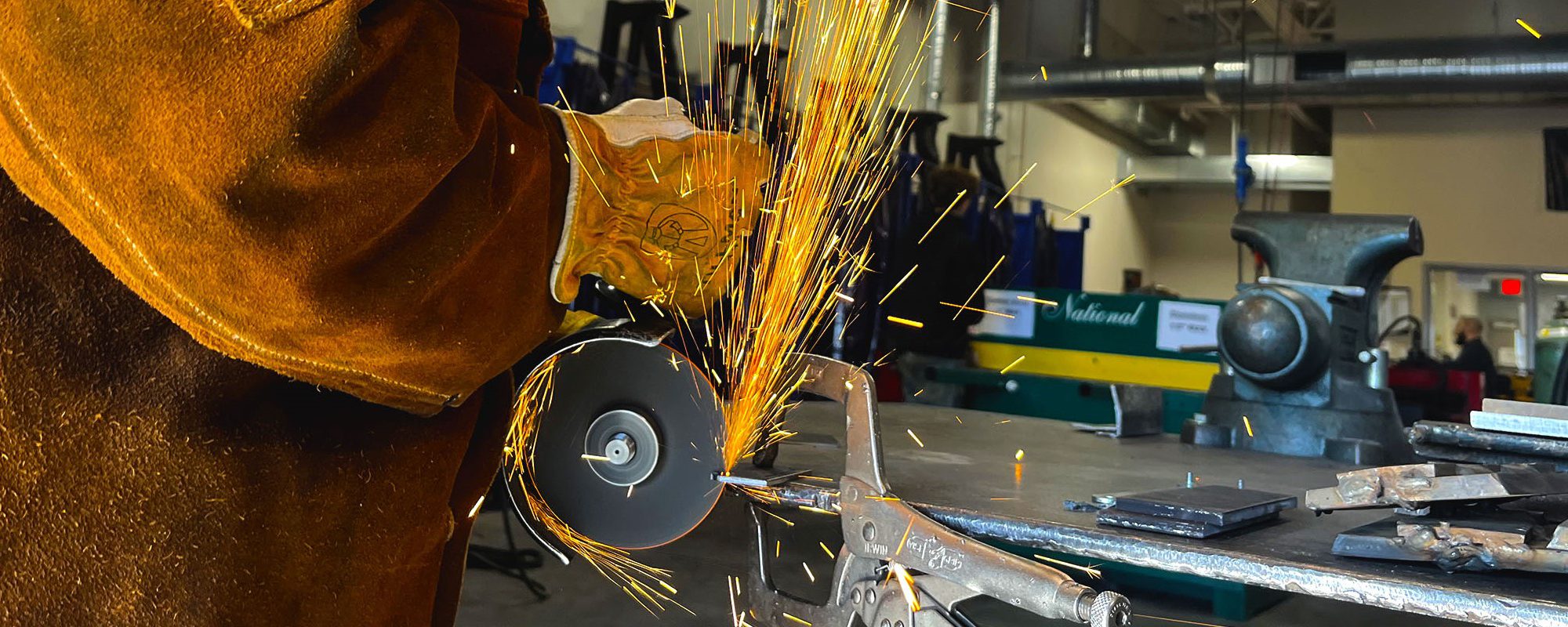 A welder's gloved hands are showered by yellow and orange sparks in the midst of a project.