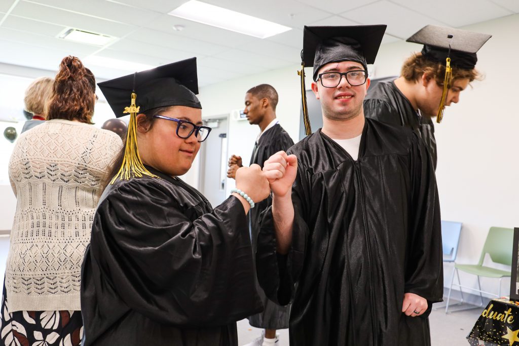 Two students in cap and gown fist bump to celebrate the coming graduation ceremony.