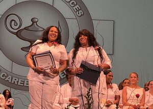 Two gradutes standing next to each other facing the camera holding award certificates.