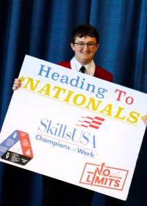 A smiling student stands facing the camera holding a poster.