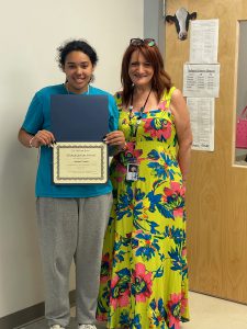 Two people standing side by sde facing the camera with one person holding a certificate.