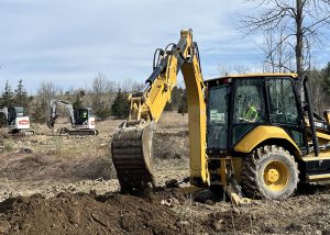 A person is in teh driver seat operating an excavator and using it to dig and scoop dirt.