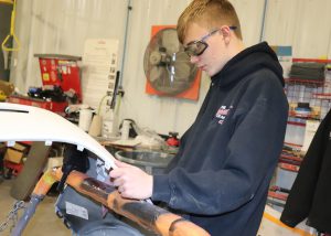 A student is wearing safety glasses and working on a piece of an autobody.