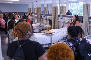 Several students standing around a hospital bed listening to a teacher speaking to them.