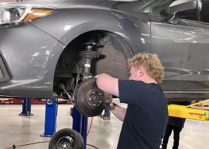 Student works on brakes of a car lifted in the air