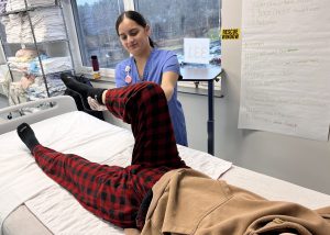 Student in scrubs flexes a patient's leg