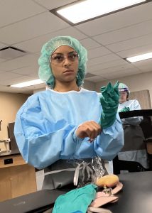 Sterile Processing student in scrubs putting a glove on