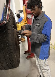 Student in uniform works on a tire.