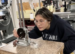 A New Visions student wearing safety glasses closely examines the settings on a machine.