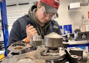 Student in red cap using a wrench on an engine