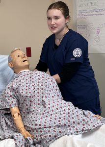 Student in nurse scrubs maneuvering a mannequin 