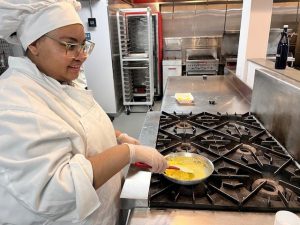 Student standing on a stove top stirring 