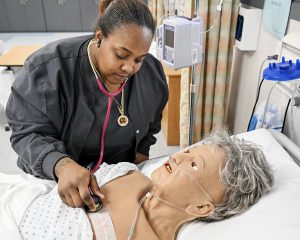 A student listens to the heart beat of a mannequin 