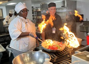 A student cooks with flames coming from the pan as a teacher looks on