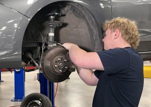 Student repairing brakes on a truck on a lift