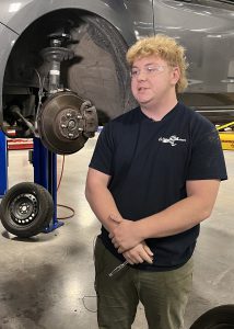 Student standing in front of a truck on a lift