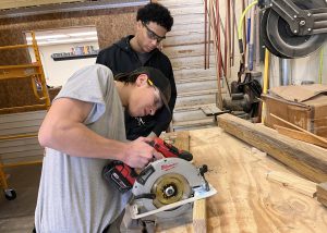 Two boys cuts a piece of wood