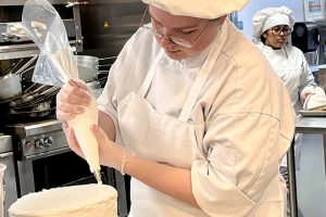 A student pipes frosting onto a cake